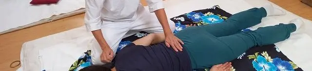 Shiatsu Krefeld: auf der Matte wird gezeigt, in dem eine Frau auf der Matte am Boden liegt und die Shiatsu Praktikerin gibt Shiatsu am Rücken.